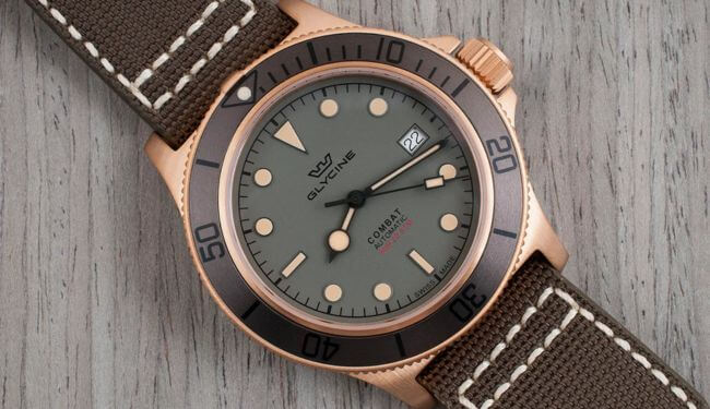 Glycine watch with a green dial and bronze-tone case on a brown leather strap, photographed on a wooden surface