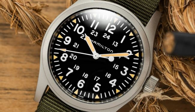 Hamilton field watch with black dial and green fabric strap on wooden background – Hamilton watch repair