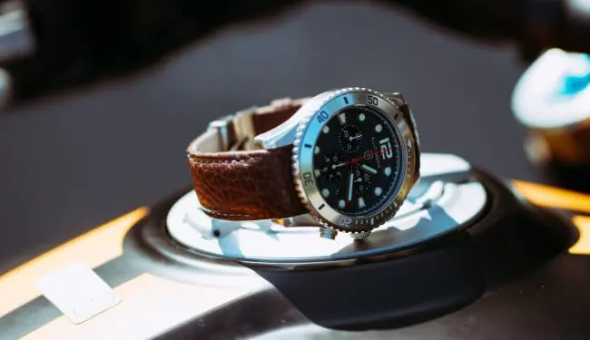 Elliot Brown watch with a dark dial and brown leather strap resting on a watch stand
