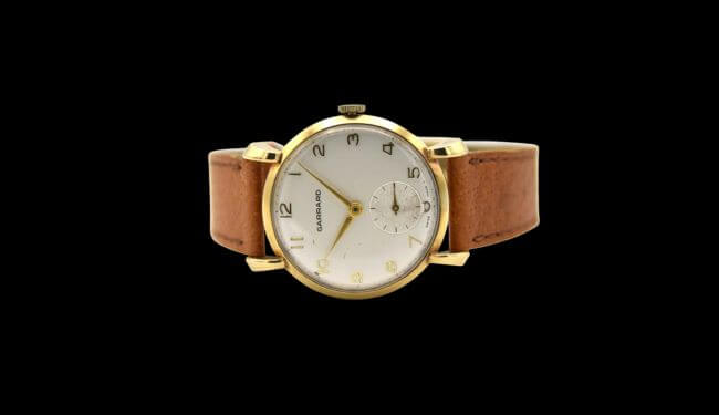 Garrard watch with a light dial and brown leather strap photographed on a black background