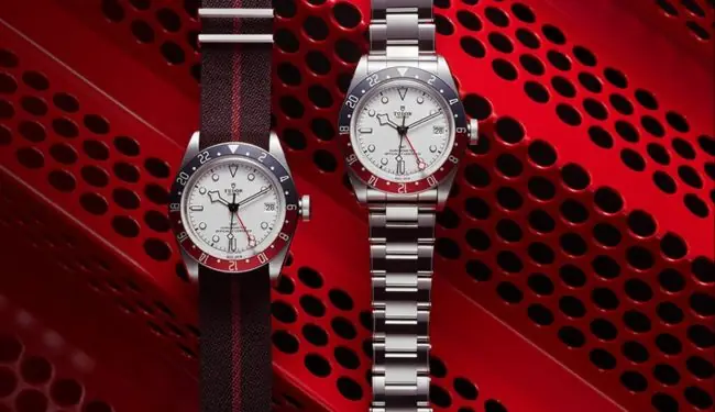 Two Tudor watches on straps against a red background