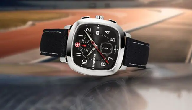 Wenger wristwatch with black dial and black strap, photographed against a blurred track background.